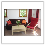 Wohnzimmer mit Sofa, Sessel und Essplatz an den Fenstern